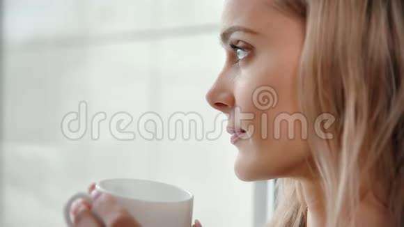 舒适的冬天微笑的女性从冰冻的玻璃中沉思喝咖啡捧杯特写视频的预览图