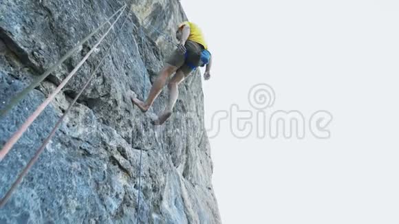 一个光着脚穿着黄色t恤在悬崖上爬下来的攀岩者笑得很满意视频的预览图