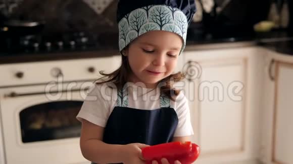 厨房里一个穿着围裙的三岁女孩带着红胡椒的肖像视频的预览图