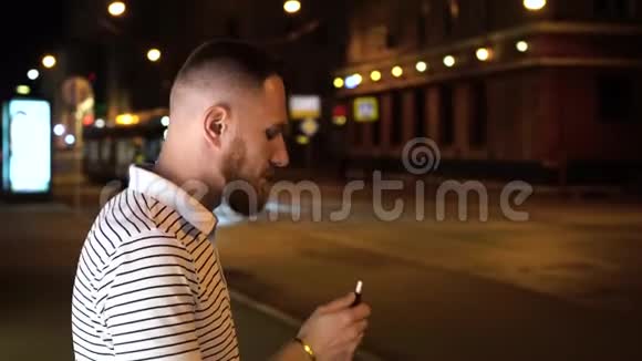 穿着条纹马球衫的胡子男晚上在街上抽烟背景是汽车视频的预览图