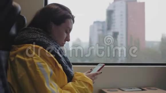 女人坐在窗边的火车上看着她的手机穿黄色雨衣的女人4k录像5994fps视频的预览图
