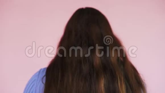 女孩在粉红色的背景上从后面露出她美丽的长姜发护发的课题慢动作视频的预览图