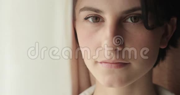 站在靠近窗户的房间里一个黑发棕色大眼睛的快乐年轻女子的特写镜头视频的预览图