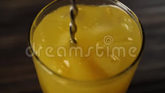 调酒师用勺子在一个高大的玻璃杯里用新鲜的橙汁搅拌冰块和木桌上的俯视图视频的预览图