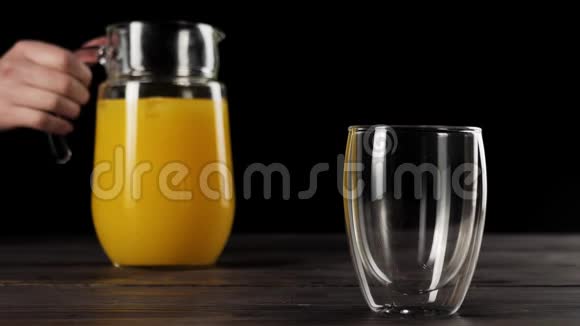 在木制桌子上用双壁玻璃中弹的女孩手拿着装饰器用冰块舀出新鲜橙汁视频的预览图