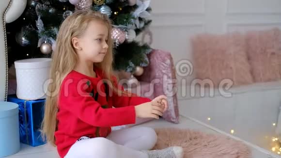 一个小女孩在家圣诞树旁打开新年礼物视频的预览图