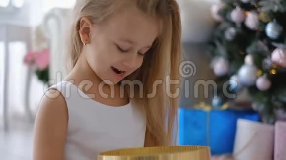 一个小女孩在家圣诞树旁打开新年礼物视频的预览图