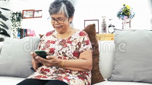 亚洲老年妇女在家里使用智能手机快乐的祖母手里拿着技术慢动作4k多莉射击视频的预览图