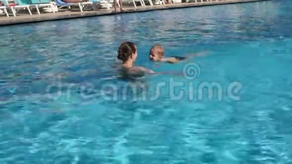 一个年轻的女人教一个孩子在晴天在游泳池里游泳视频的预览图