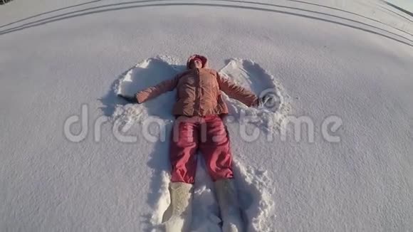 一个穿着桃色夹克和粉红色裤子的女人躺在雪堆里做一个雪天使霜冻的晴天慢动作视频的预览图
