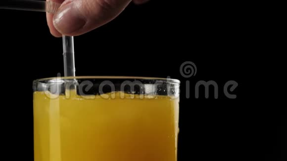 侧视女孩手与鸡尾酒吸管搅拌冰块与新鲜橙汁在一个高玻璃在黑色背景下视频的预览图