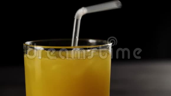 鸡尾酒吸管落在新鲜橙汁中的侧面视图冰块在黑色背景下的高杯中视频的预览图