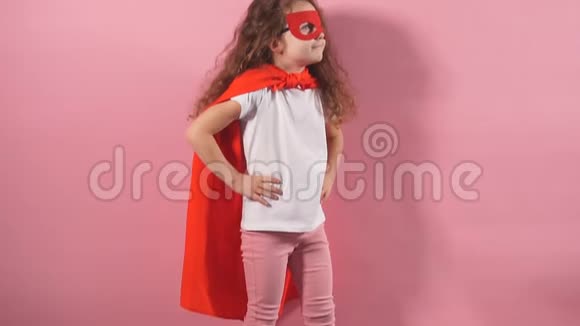 漂亮可爱的孩子穿着红色超级英雄套装戴着面具站在粉红色背景的旁边视频的预览图