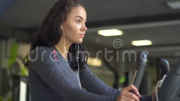 一个年轻漂亮的女孩戴着耳机坐在健身车上的肖像视频的预览图