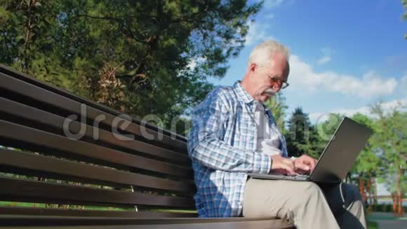 在公园里坐在长凳上用电脑打字的老人视频的预览图