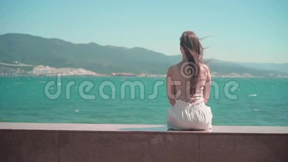 一个穿着白色短裤和T恤的女孩沿着城市长廊散步一个女孩坐在河堤的花岗岩栅栏上视频的预览图