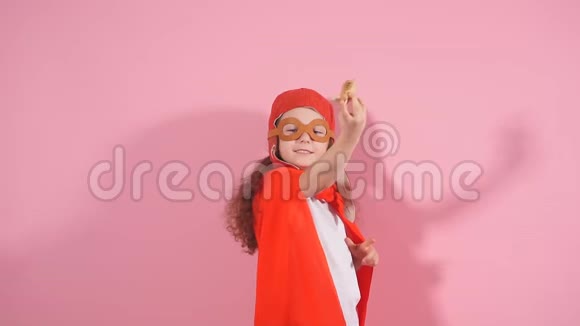 漂亮的女孩穿着红色斗篷戴着飞行员头盔举起双手手持木制玩具飞机视频的预览图