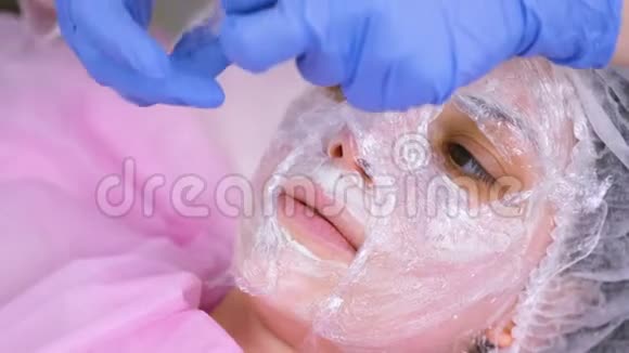 美容师把一层塑料薄膜贴在女士脸上的保湿面膜上面视频的预览图