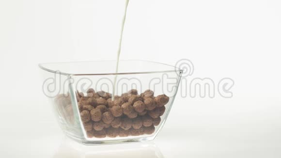 新鲜健康食品牛奶倒入透明的碗中白色背景上有巧克力麦片球视频的预览图