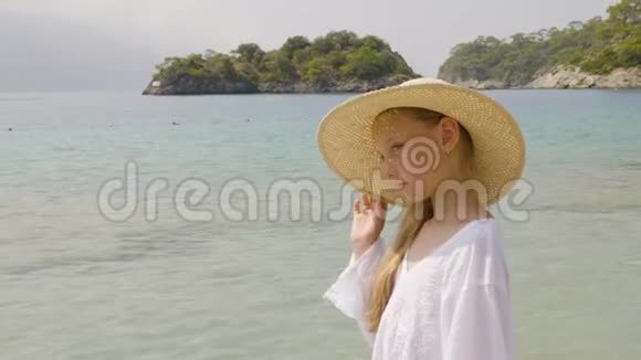 天堂海滩上戴草帽的可爱女孩肖像少女在夏日海滩阳光明媚的日子眯着眼睛年轻模特视频的预览图