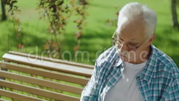 愤怒的老人在公园的长凳上打电话视频的预览图