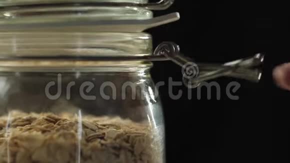 新鲜健康食品手打开一个装有燕麦麦片的罐子放在木桌上把燕麦麦片倒入靠近一杯牛奶的绿色碗里视频的预览图
