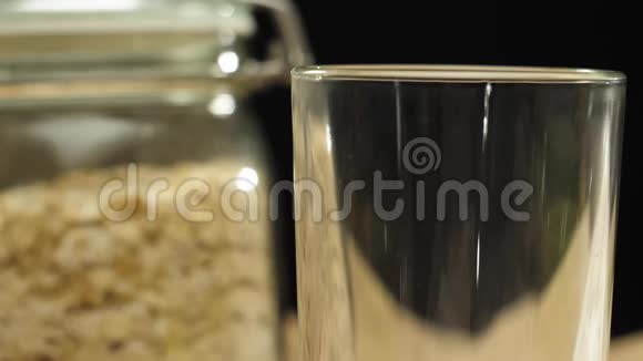 新鲜健康食品牛奶倒入透明玻璃附近的透明罐子与燕麦谷类在黑色背景概念视频的预览图