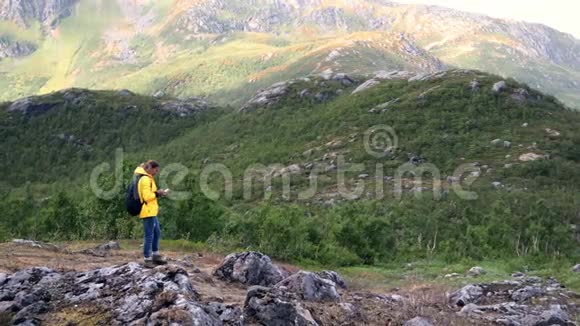 年轻女性旅行者站在山上用她的智能手机视频的预览图