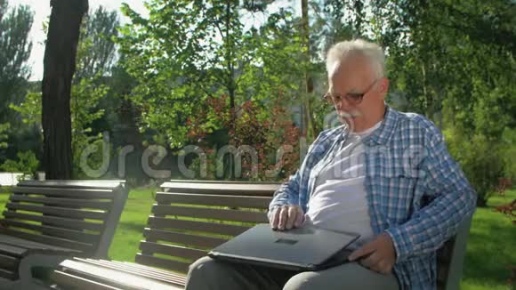 一个年长的人坐在长凳上花园里有一台笔记本电脑视频的预览图