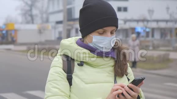 冠状病毒保护一位戴着医用防护面罩的年轻女性站在欧洲的一条城市街道上手里拿着智能手机视频的预览图