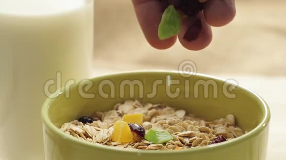 新鲜健康食品手把蜜饯葡萄干和蔓越莓倒在靠近玻璃的绿色碗里放在黄色的燕麦麦片上视频的预览图