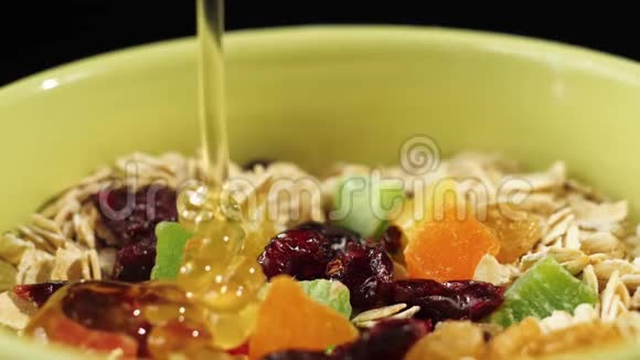 新鲜健康食品金色的蜂蜜在一个绿色的碗里用蜜饯葡萄干和蔓越莓倒在燕麦片上视频的预览图