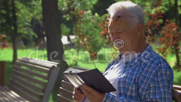 侧面看一个有胡子的老人正在看书中读有趣的时刻老人坐在公园的长凳上看书视频的预览图