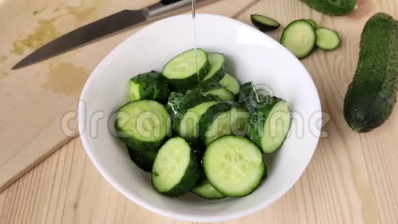 切片黄瓜在白碗中倒入油新鲜有机绿色蔬菜烹饪健康饮食食品特写木制桌子视频的预览图