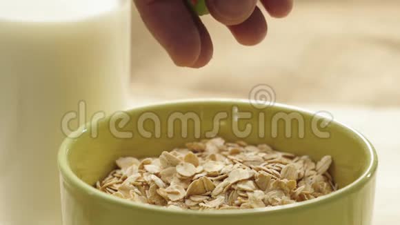 新鲜健康食品手把多种颜色的蜜饯倒在黄燕麦谷类食品上放在一个绿色的碗里靠近玻璃杯放白色牛奶视频的预览图