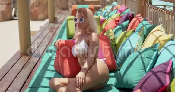 穿着泳装躺在五颜六色的枕头上在开放式木制露台上放松的女士视频的预览图