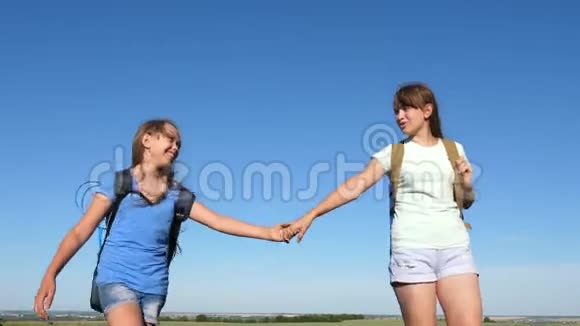女旅行者穿过田野夏天在草地上远足的女孩女孩们女游客牵着手走视频的预览图