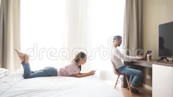 年轻漂亮的夫妇在卧室里休息男人坐在电脑前在家工作视频的预览图