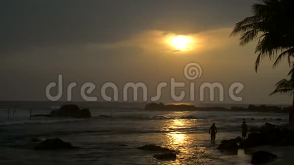 日落时沿着海滨散步的两个人的剪影视频的预览图