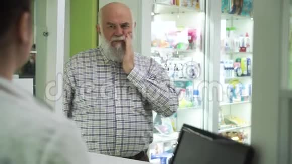 牙疼的老胡子男人来到药房年轻女药师为顾客提供止痛药物视频的预览图