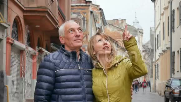 一对有年龄差异的幸福浪漫情侣的肖像拥抱并指向古城的户外事物视频的预览图