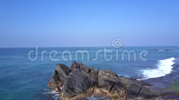 年轻女子坐在巨大的岩石悬崖上靠在无尽的海洋上视频的预览图