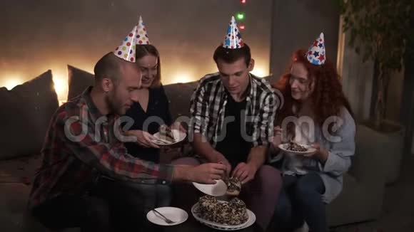积极的男人在黑暗中装饰着花环灯房坐在沙发上吃着节日的生日蛋糕生日男孩视频的预览图