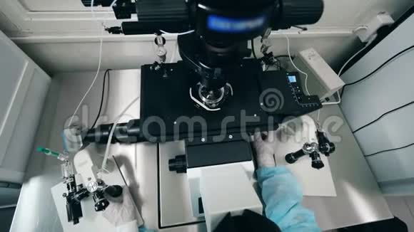 现代显微镜和操作显微镜的实验室工作人员的俯视图视频的预览图