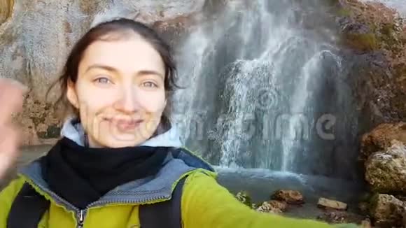 有趣的十几岁女孩做了一个有趣的自拍而旅行的背景是一个美丽的瀑布她做鬼脸做鬼脸视频的预览图