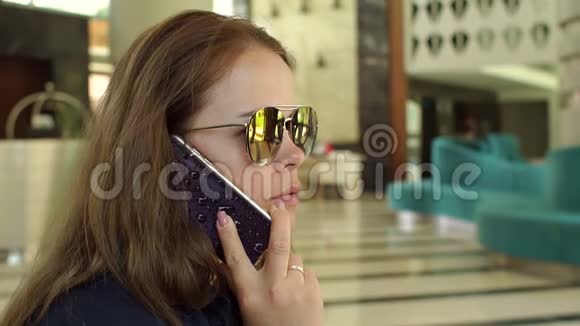 一个戴着太阳镜的年轻女孩坐在酒店大厅里打电话视频的预览图