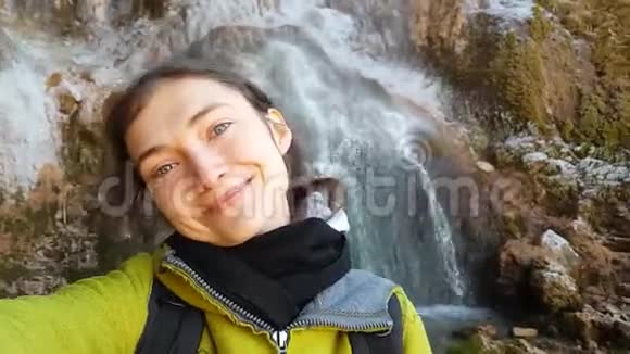 布鲁内特旅行女孩在美丽的瀑布背景上自拍一个带背包的旅行者视频的预览图
