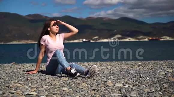 穿粉红色t恤的年轻迷人的女孩或年轻女子在沙滩上把遮阳板放在手上然后移开视线视频的预览图