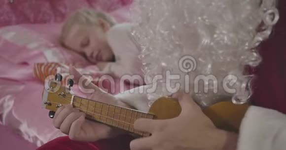 特写圣诞老人的双手演奏四弦琴小金发女孩在后台醒来父亲唤醒了他视频的预览图