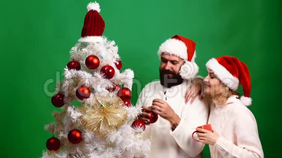 一对戴着红色圣诞帽的夫妇在绿色背景上装饰圣诞树家庭圣诞节寒假和视频的预览图